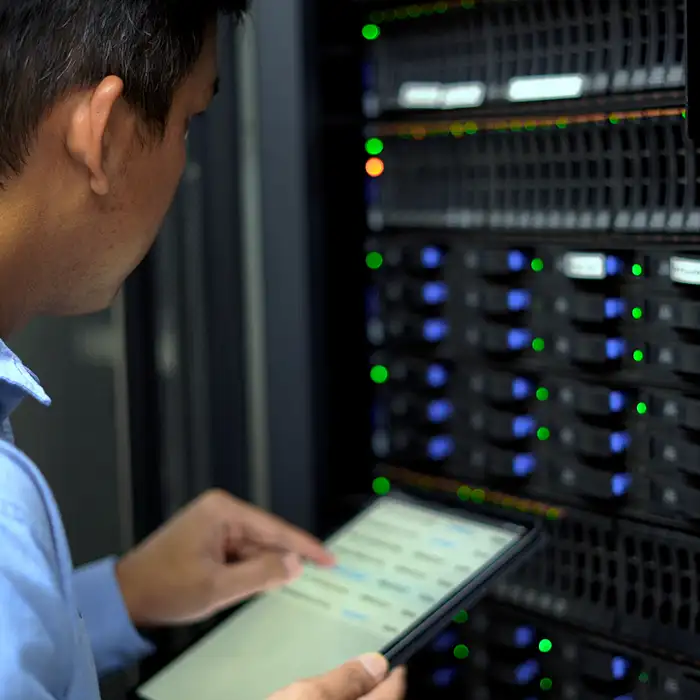 man looking at tablet while working in front of data center switchboard